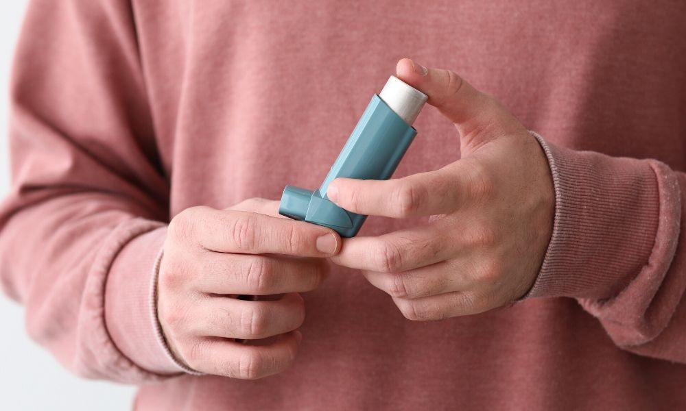 An adult wearing a salon-colored sweater holding an inhaler.
